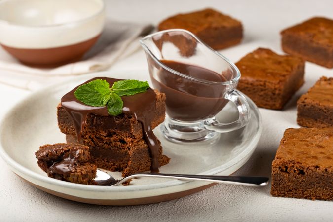 Brownies on plate with spoon served with sauce and mint garnish