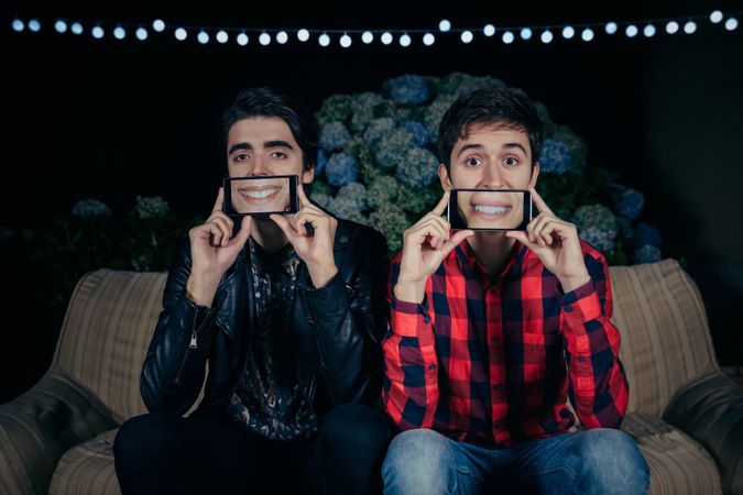 Funny young men holding smartphones showing female mouths smiling