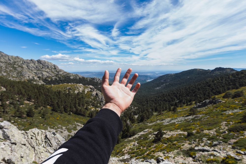 Person stretching hand to blue sky above mountain valley