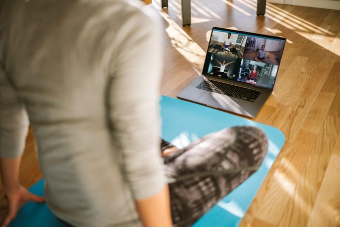 View from back of woman having virtual yoga class with group of people at home on a video conference