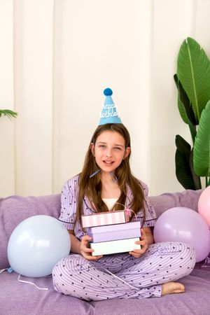 Young girl celebrating birthday at home with presents and balloons.