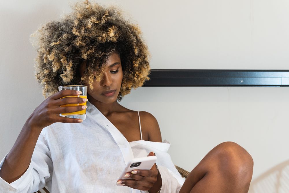 Black woman sitting on armchair and surfing smartphone