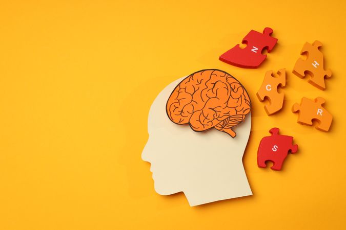 Cut out of head shape with brain & puzzle pieces on orange background, copy space
