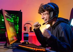 Young man plays the computer and celebrates victory in video game with a clenched fist and a smile.