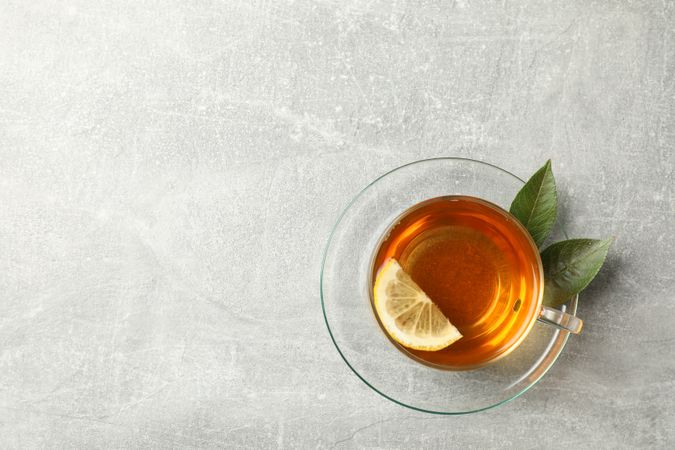 Cup of tea, mint and lemon on grey background, top view