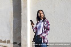 Female standing in the sun in front of wall holding phone 0Jr2n0