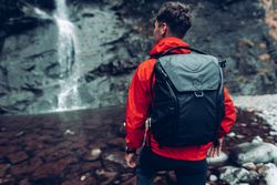 Back view of a man in red jacket with backpack standing against waterfalls 41AED4