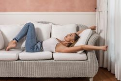 Woman in casual outwear laying on couch stretching her arms