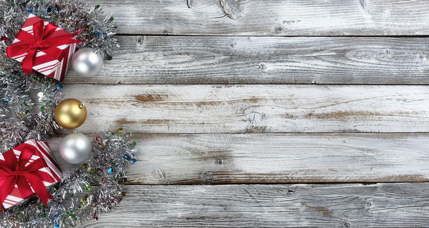 Traditional gold and silver balls, plus gifts surrounded by tinsel on a wood background for the Christmas or New Year holiday season