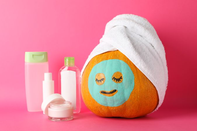 Funny pumpkin and skin care accessories on pink background, space for text