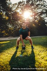Vertical shot of strong young man exercising with kettle bell weights in the park 4AGDz0