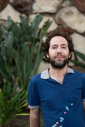 Portrait of man smiling and looking at camera in front of stone wall and plant