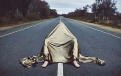 Man sitting in center of road under gold sheet