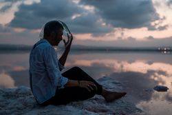 Man with fish tank on head sitting at seashore