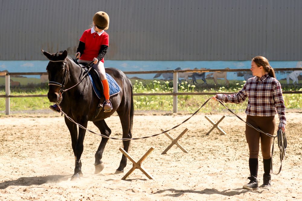 Young rider practices horseback skills with instructor's guidance.