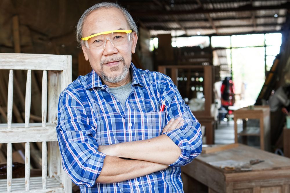 Man in safety glasses and plaid shirt in woodshop