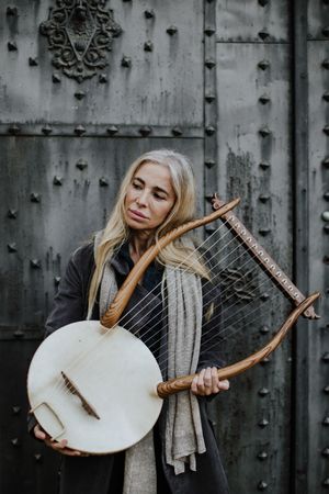 Pensive charming woman holding lyre at metal gates