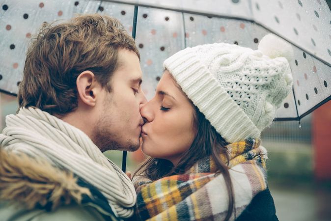 Side view of couple kissing on cold day under umbrella