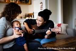 Mother playing acoustic guitar for baby and partner 5wnz90