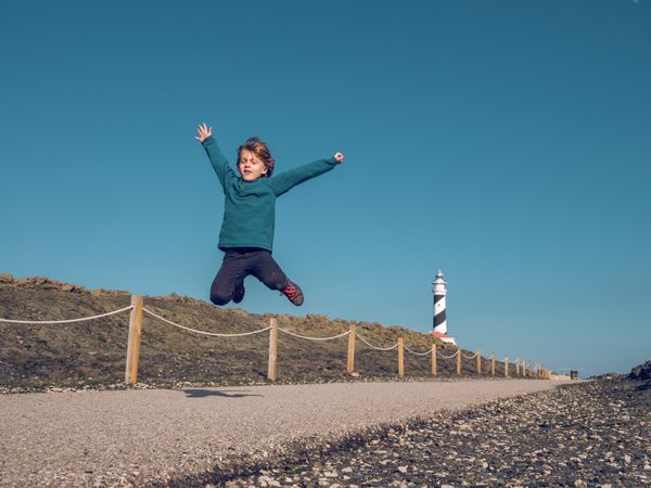 Boy jumping against lighthouse in countryside