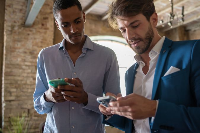 Two young businesspeople holding smartphones and talking together in the office
