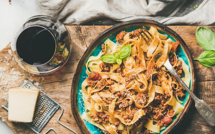 Pasta dinner with minced meat, cheese and red wine on wooden board, horizontal composition