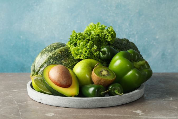 Tray with green fruits and vegetables on gray table