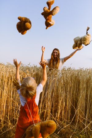 Mother throwing teddy bears to Little boy on field in countryside