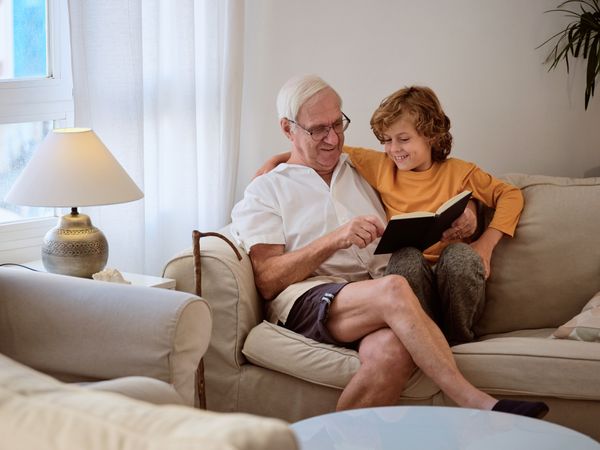 Mature male reading book with grandson in living room