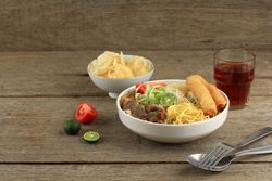 Dinner of Indonesian beef noodle soup with noodles, beef, spring roll, cabbage and tomato
