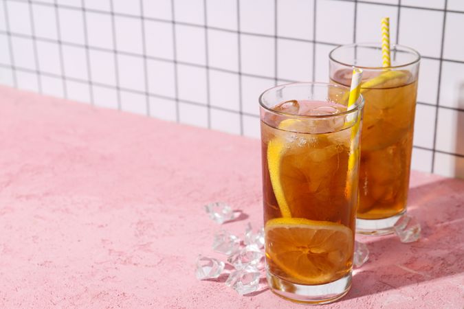 A glass of cold tea with ice and an orange on a pink background