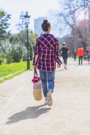 Rear view of a young hipster woman walking in a park in sunny day while holding a wicked basket