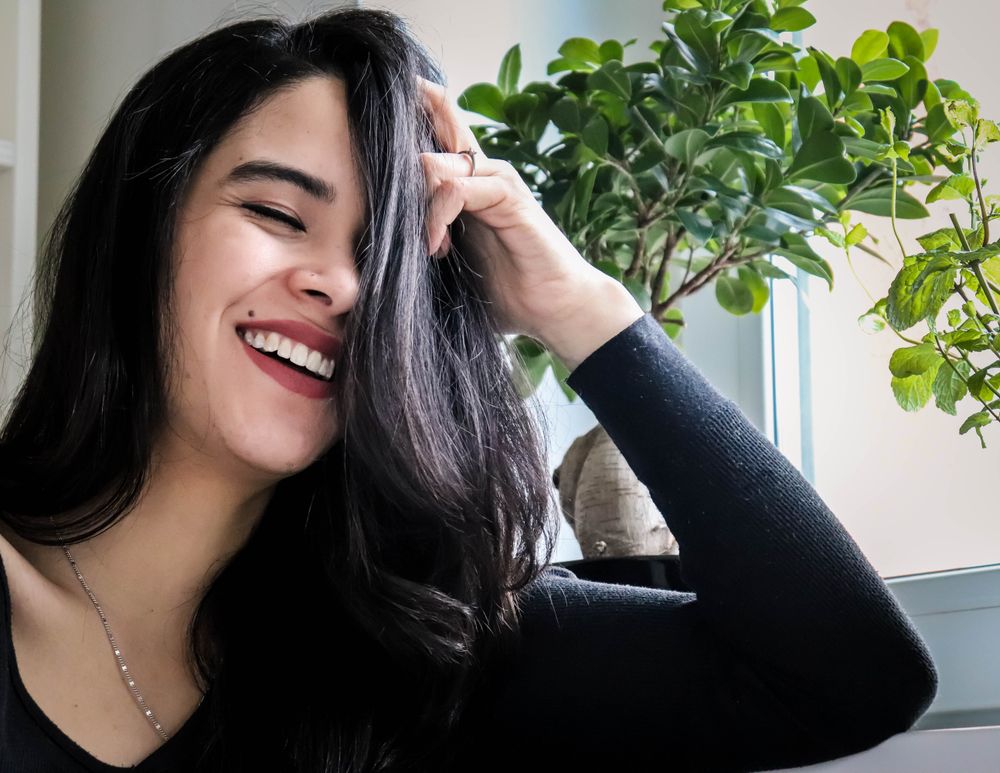Portrait of woman in long sleeve shirt holding her hair and smiling