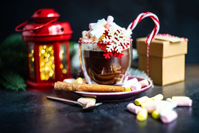 Side view of marshmallow hot chocolate on table with red lantern and gift
