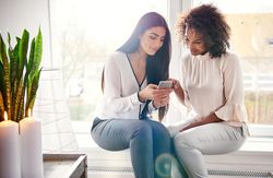 Two woman looking at a smartphone together by the window
