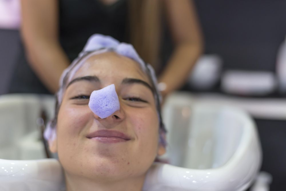 Funny female lying back with purple suds in her hair and on her nose