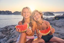 Smiling children with watermelon slices on coast near sea