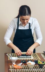 Female chef in apron rolling sushi in traditional mat 0vvnd0