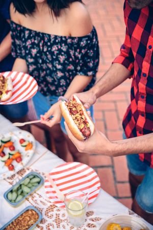 Man in red plaid holding hot dog at barbecue with friends