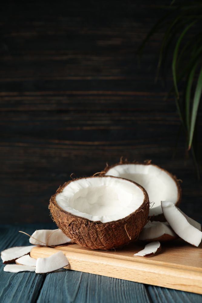 Board with coconut on wooden background, space for text