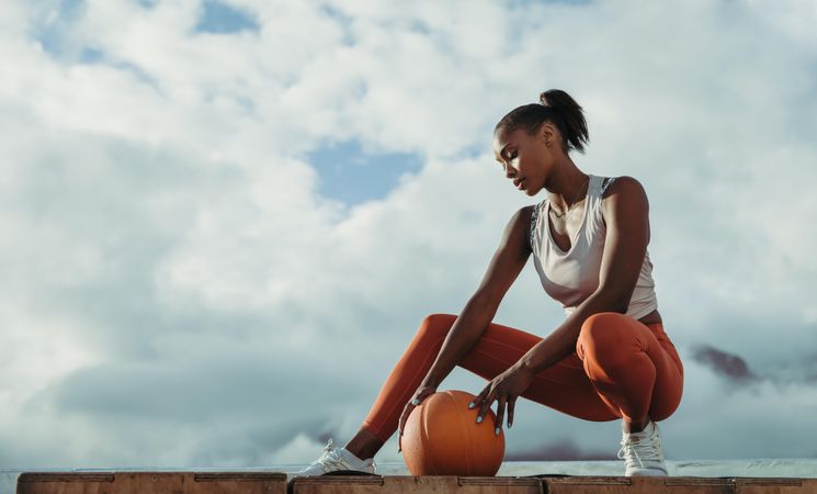 Fit woman bending low with medicine ball against cloudy sky