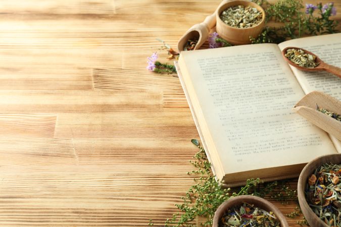 Book, herbs in bowls and scoops on wooden background, space for text