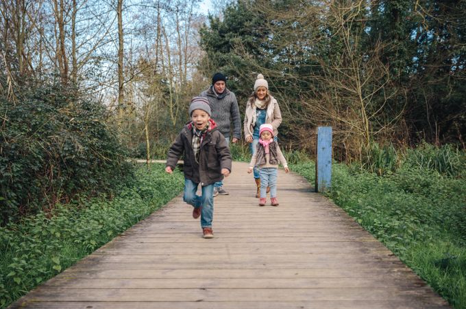 Little boy running ahead of parents and sister on forest path