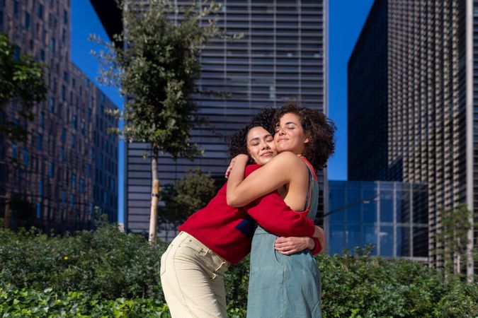 Female couple hugging each other in city park with office buildings in background