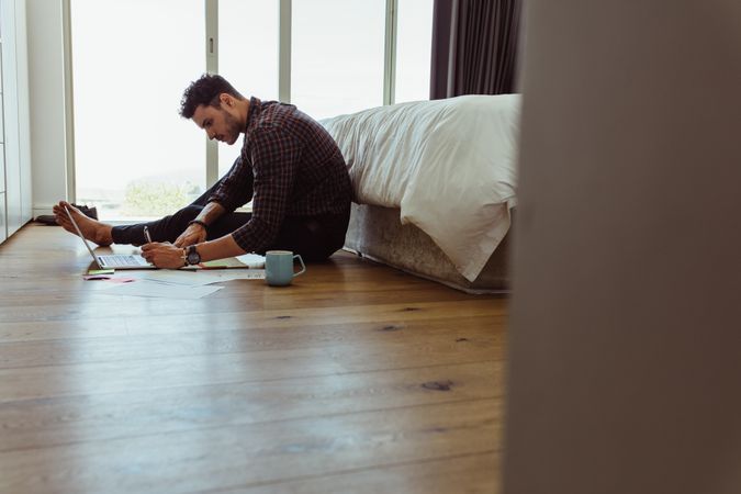 Man working hard from home taking notes at the foot of his bed