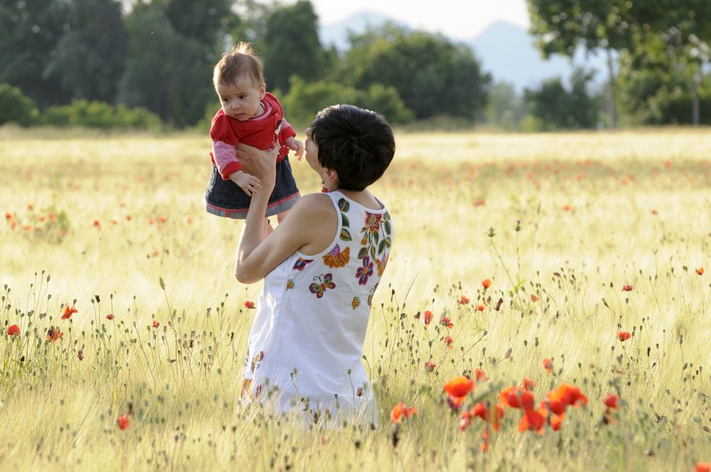 Woman holding up baby girl in field