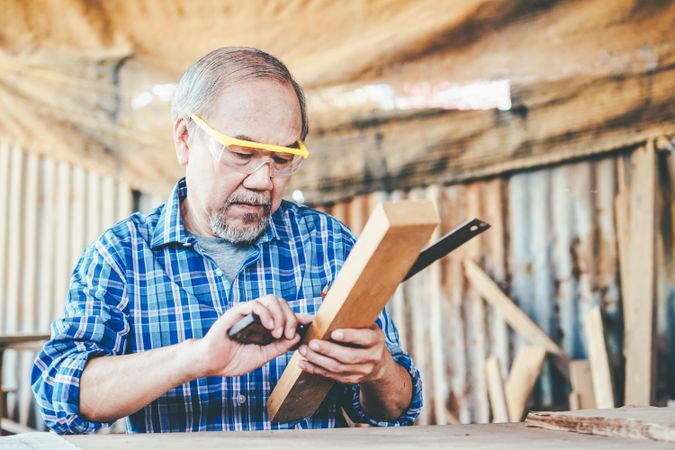 Older man measuring piece of wood in shop