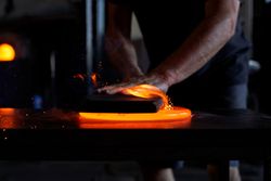Hands of male worker cutting hot glass at table