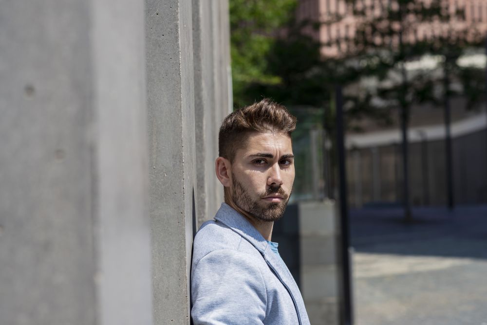 Side view of man leaning on wall outside looking at the camera
