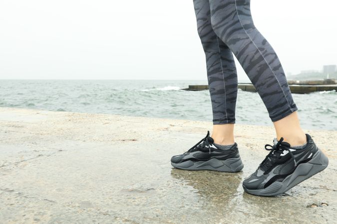 Female legs in leggings and sneakers on sea pier, space for text